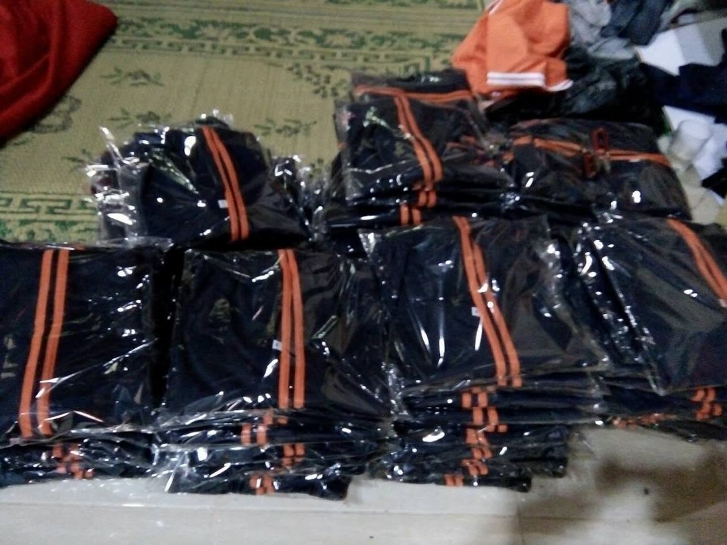 Tumpukan produk pakaian; sebagian terbungkus plastik. Jumlah pesanan dan kesiapan kirim tidak dapat dipastikan dari foto.