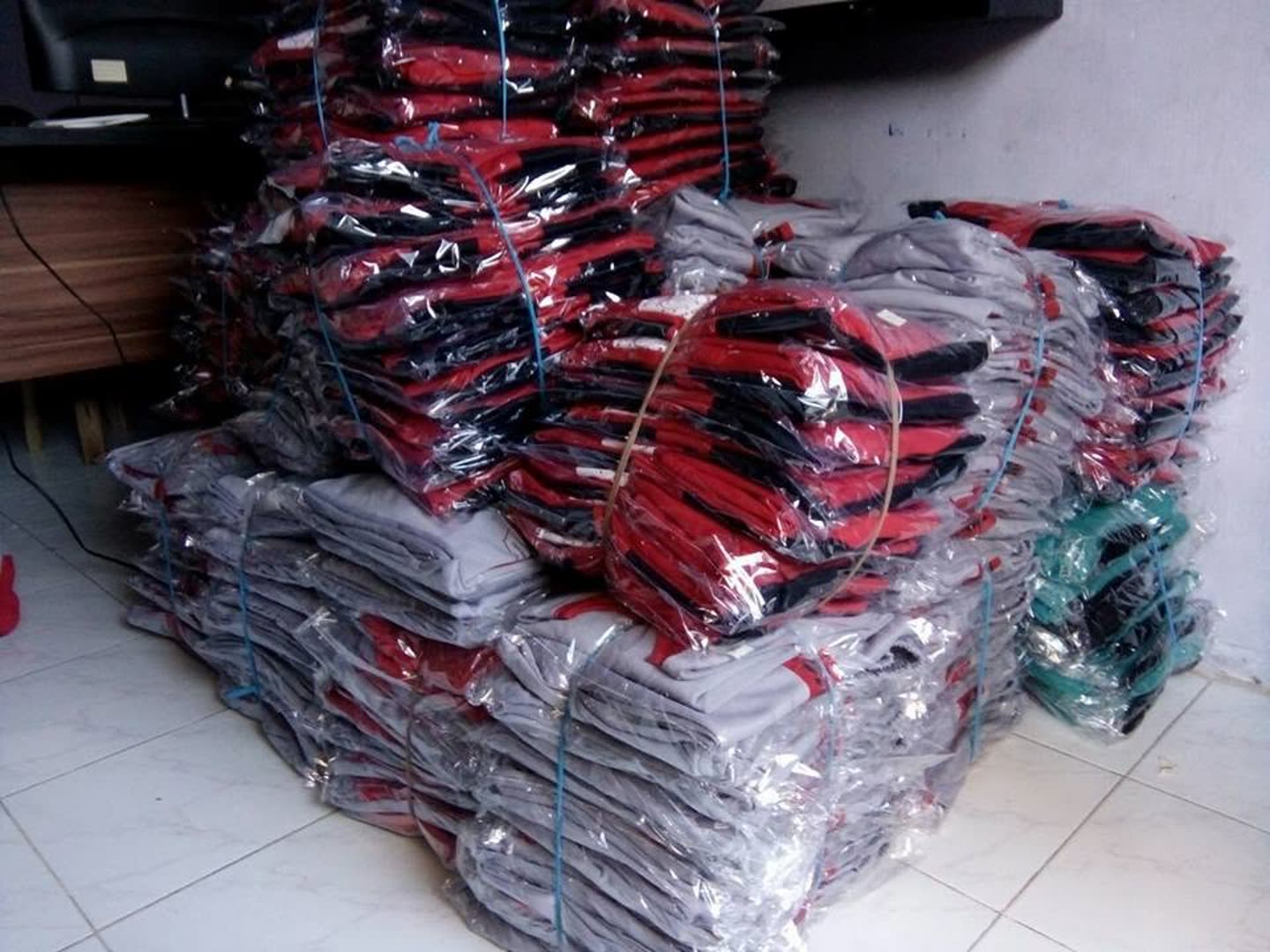 Tumpukan produk pakaian; sebagian terbungkus plastik. Jumlah pesanan dan kesiapan kirim tidak dapat dipastikan dari foto.