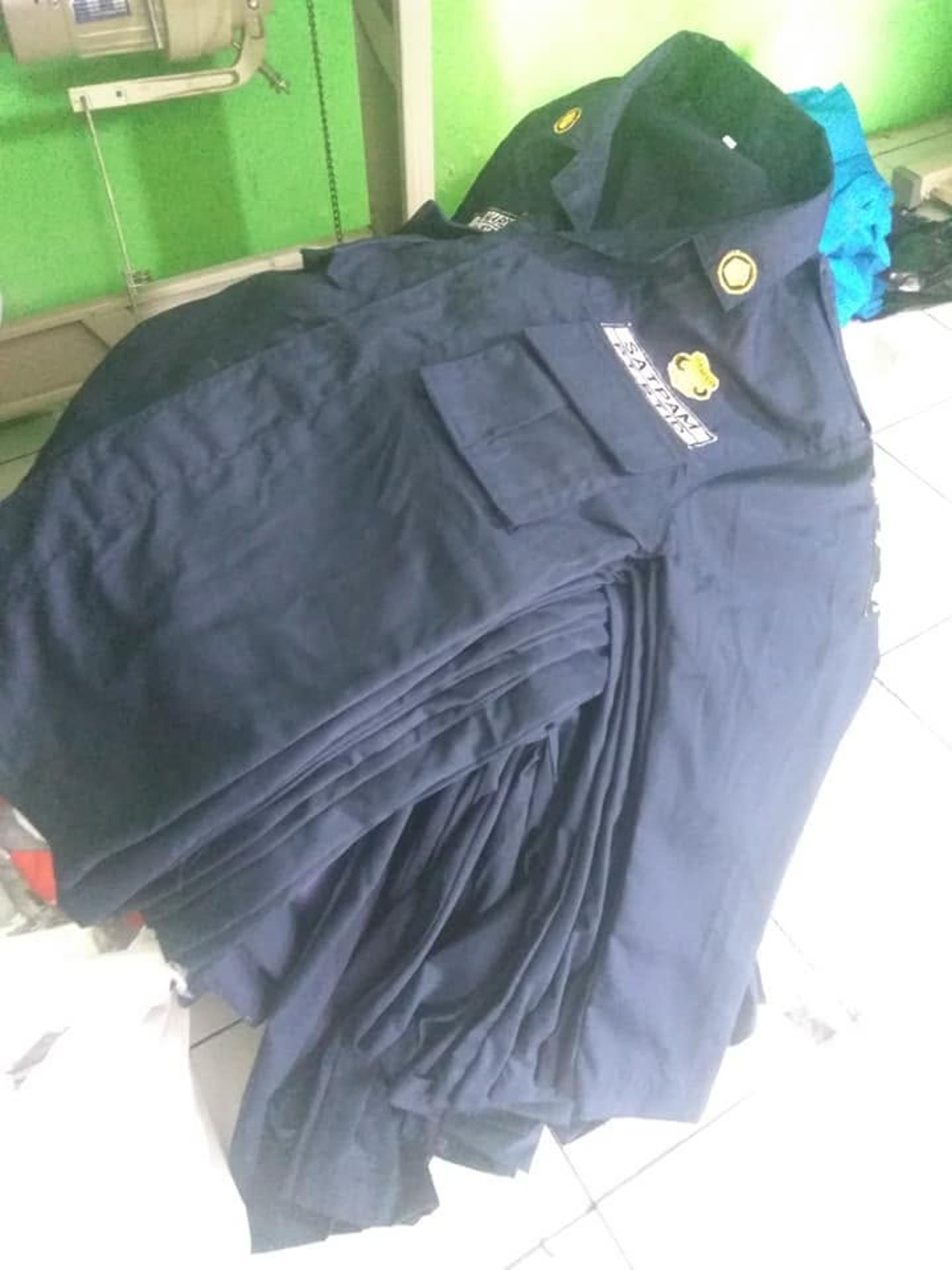 Tumpukan kemeja gelap dengan tanda/logo pada dada.