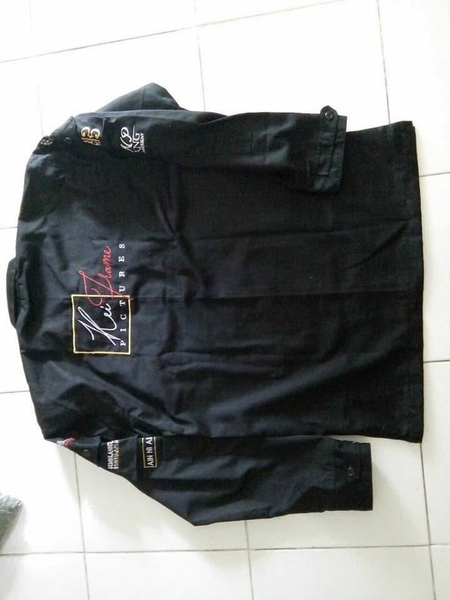 Kemeja hitam lengan panjang dengan beberapa saku dan tulisan.