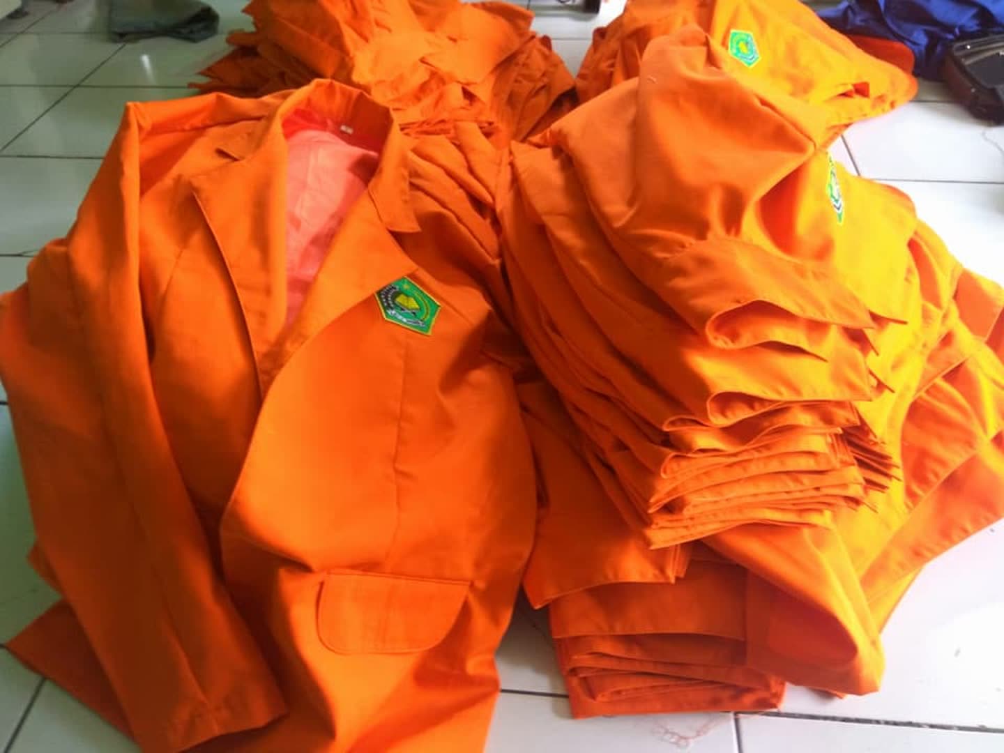 Tumpukan kemeja oranye dengan logo dada.
