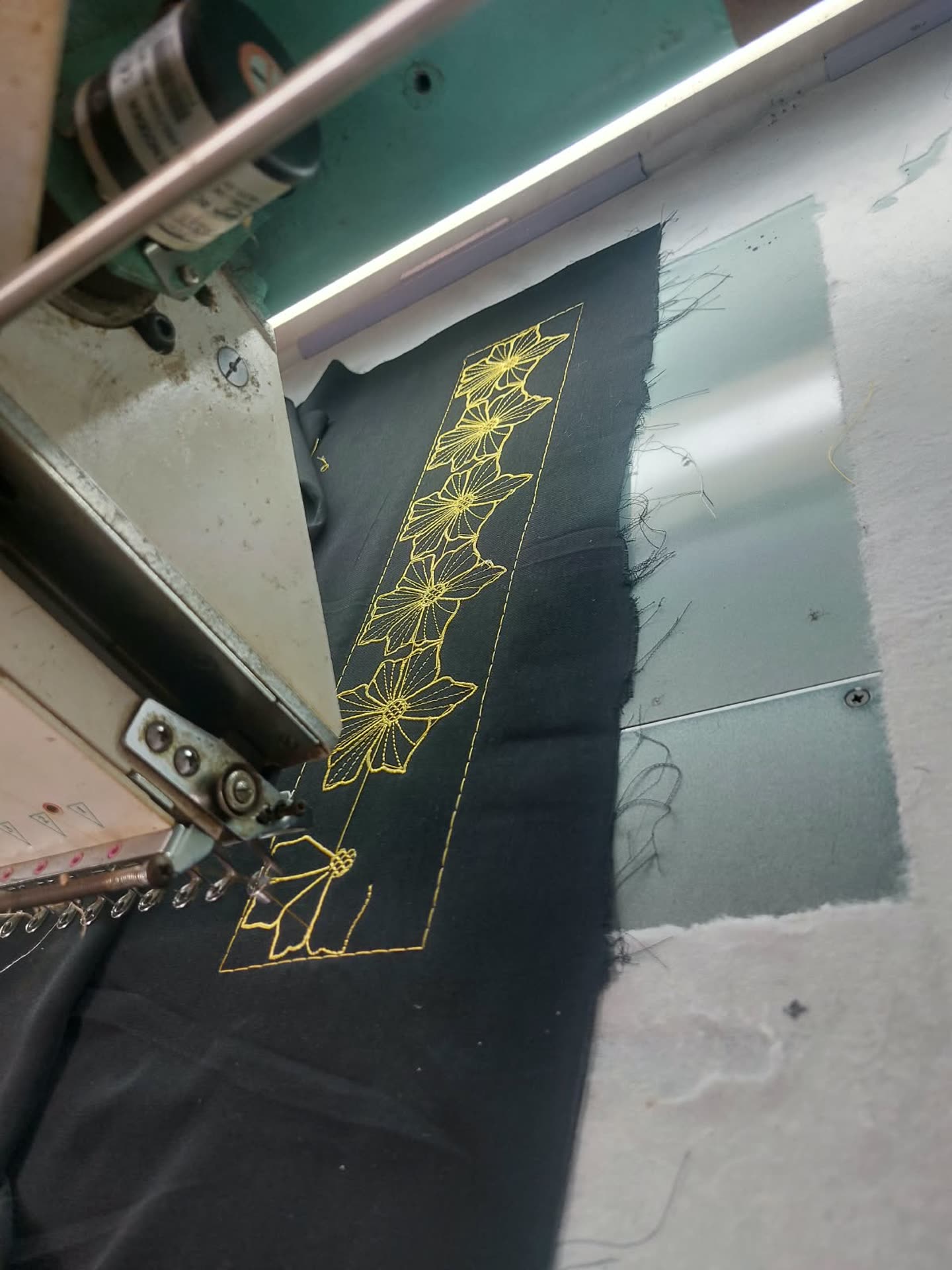 Motif geometris kuning pada kain gelap di mesin bordir.