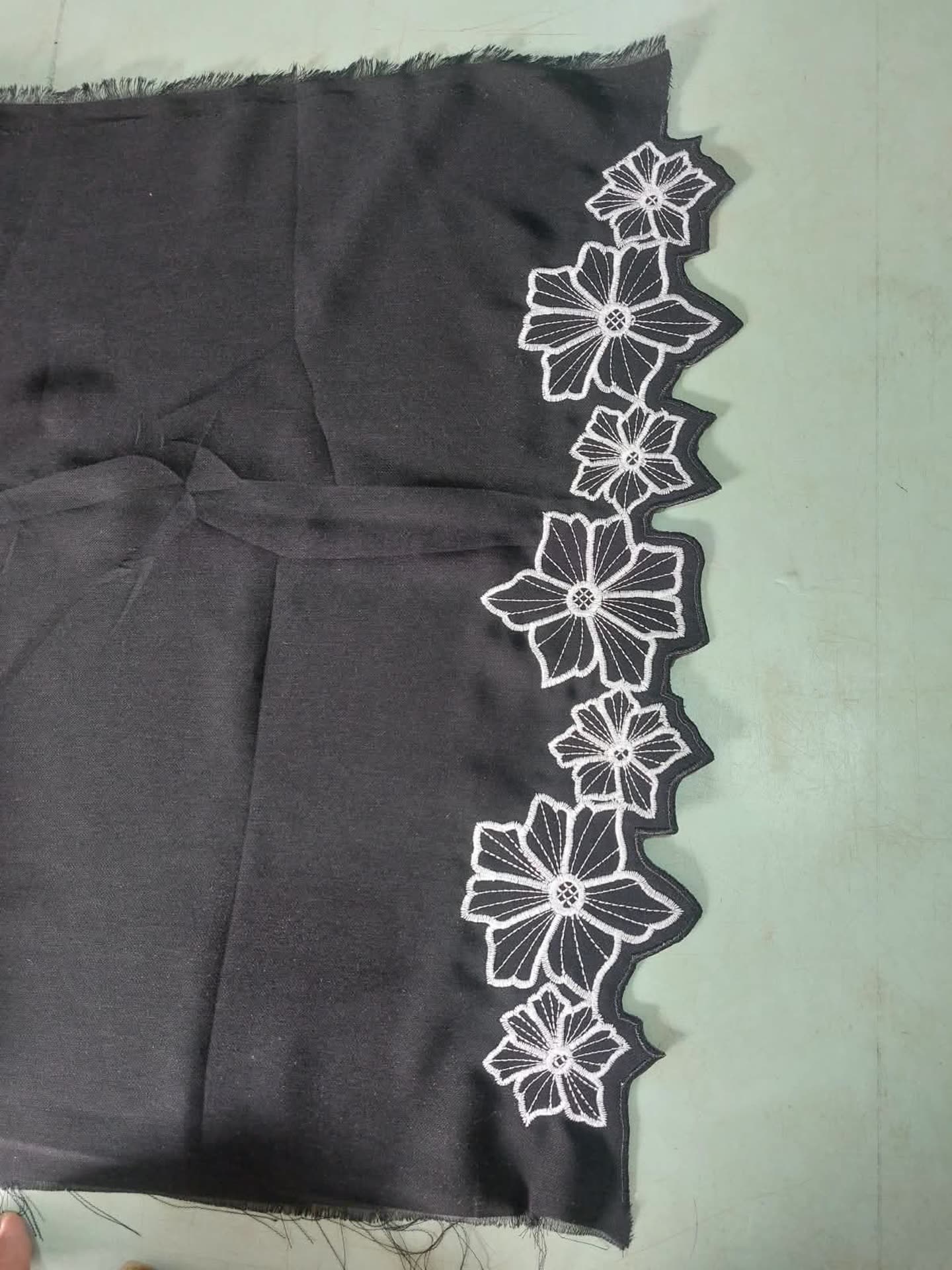 Motif bordir geometris putih sepanjang tepi kain gelap.