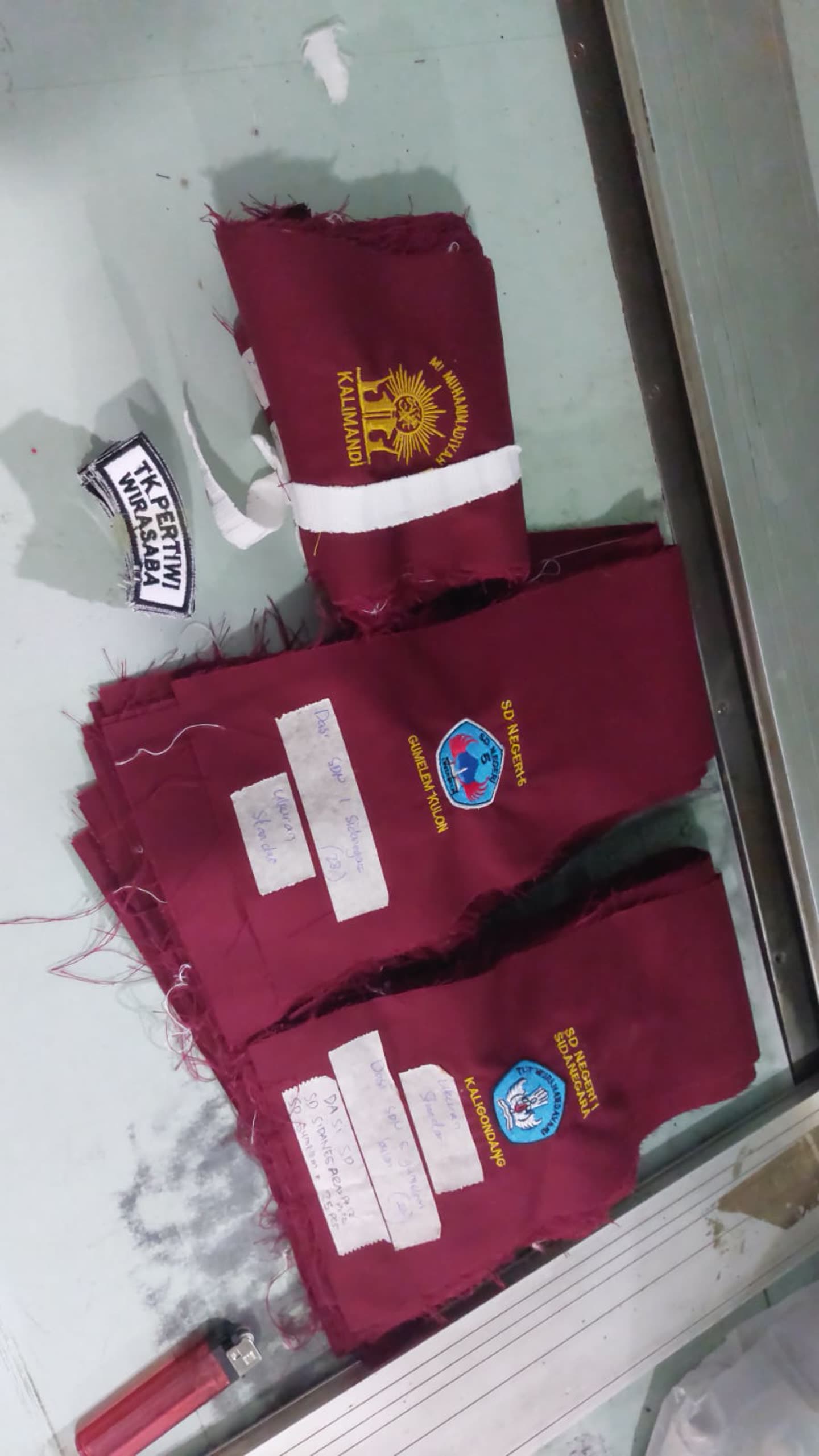 Tumpukan produk kain marun dengan logo dan label kertas.
