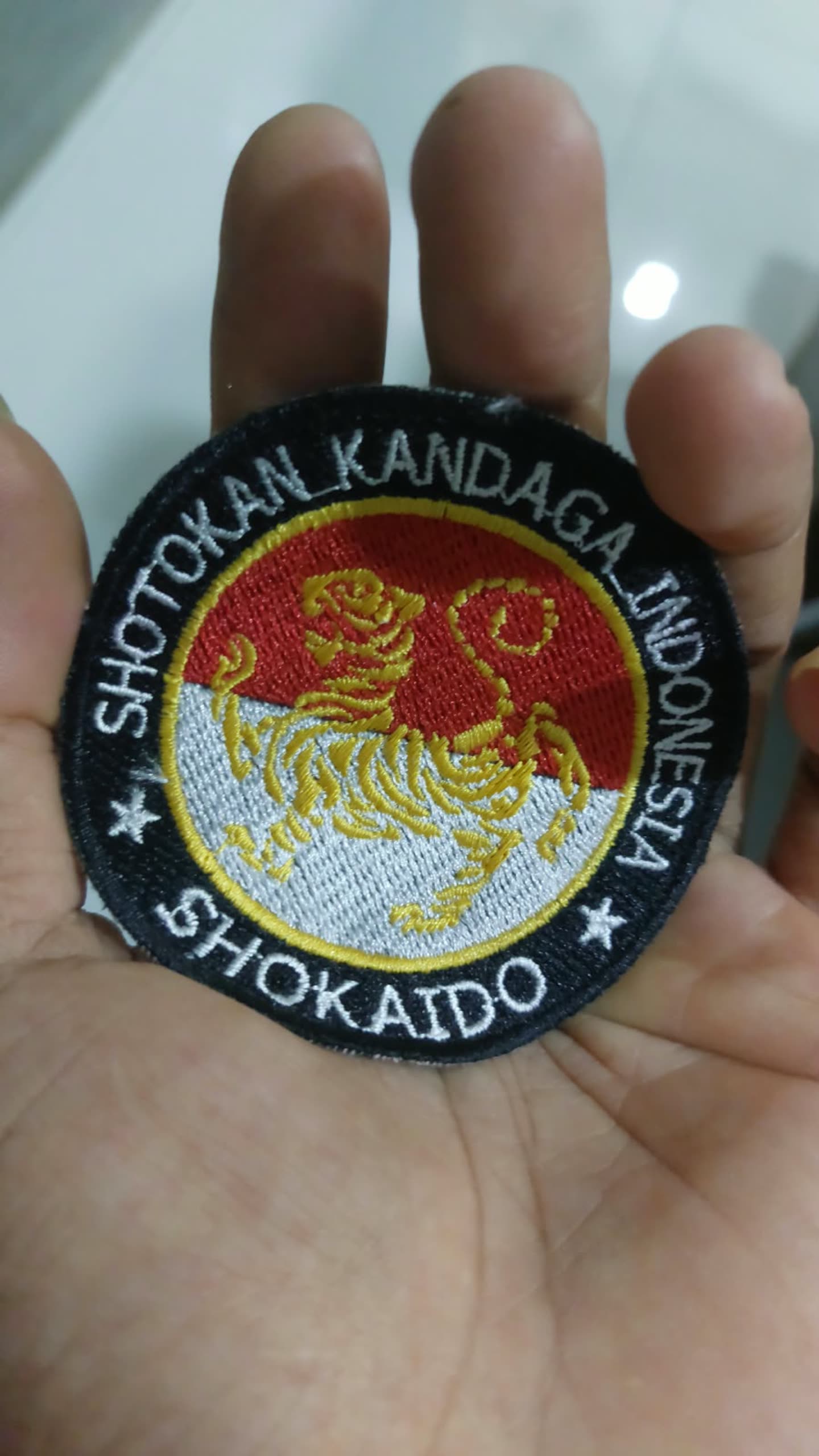 Emblem bundar dengan tulisan pada tepi, di tangan.